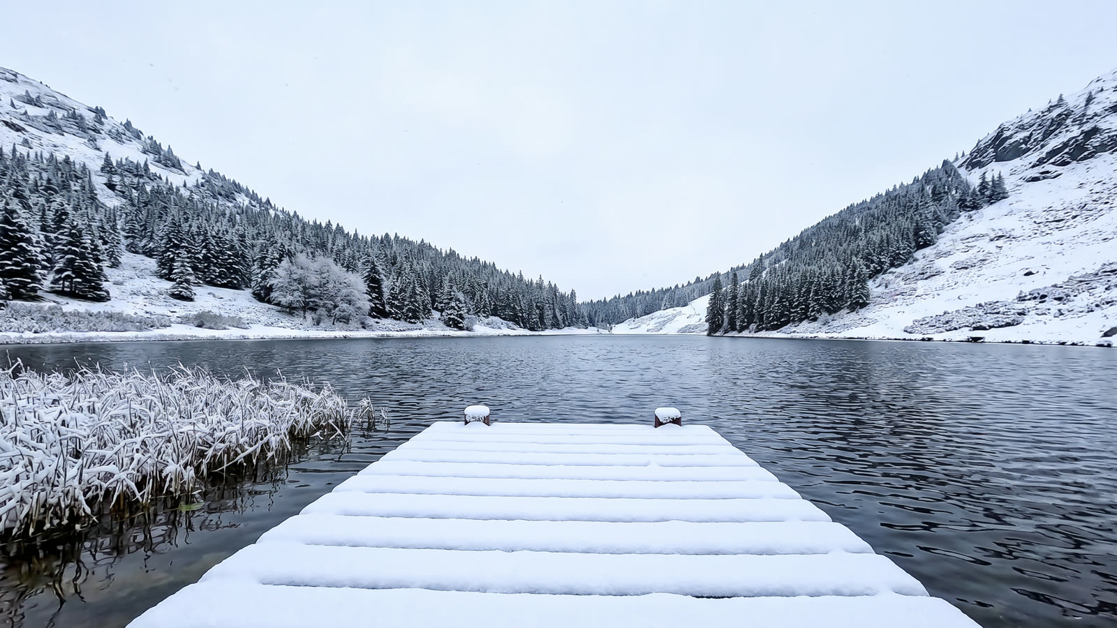 The source clip's first frame, edited into a snowy winter day: snow on the dock, the hills and the pines, frost on the reeds, the lake still open water
