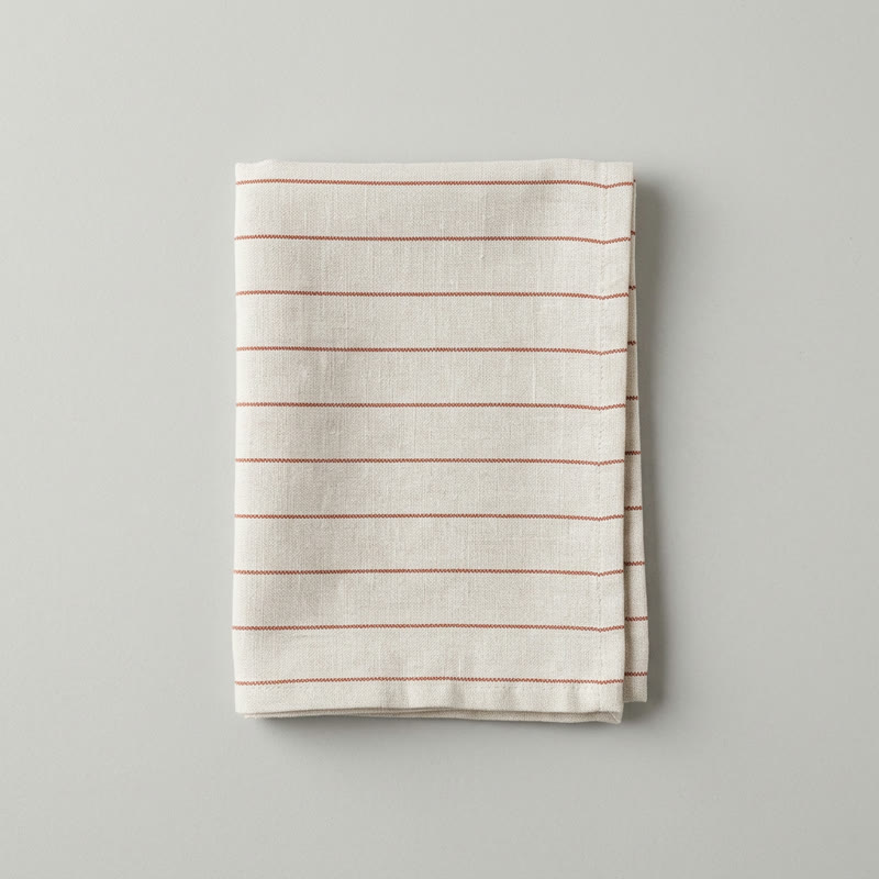 A folded linen napkin with thin rust-red stripes on a light grey background