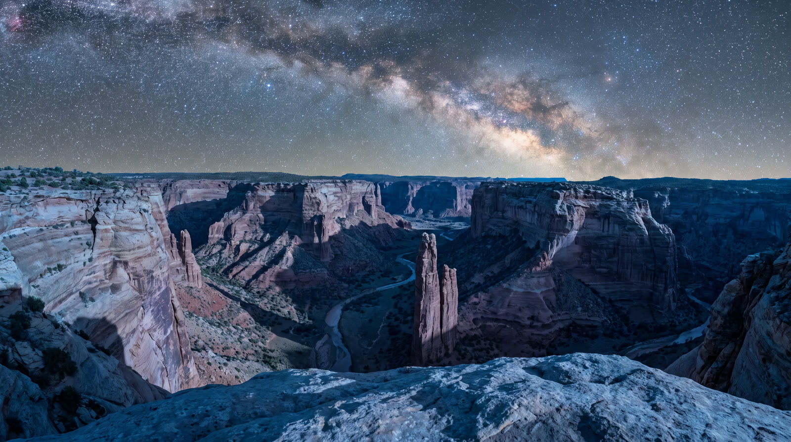 A desert sandstone canyon at night seen from a rock ledge, the Milky Way above the canyon walls