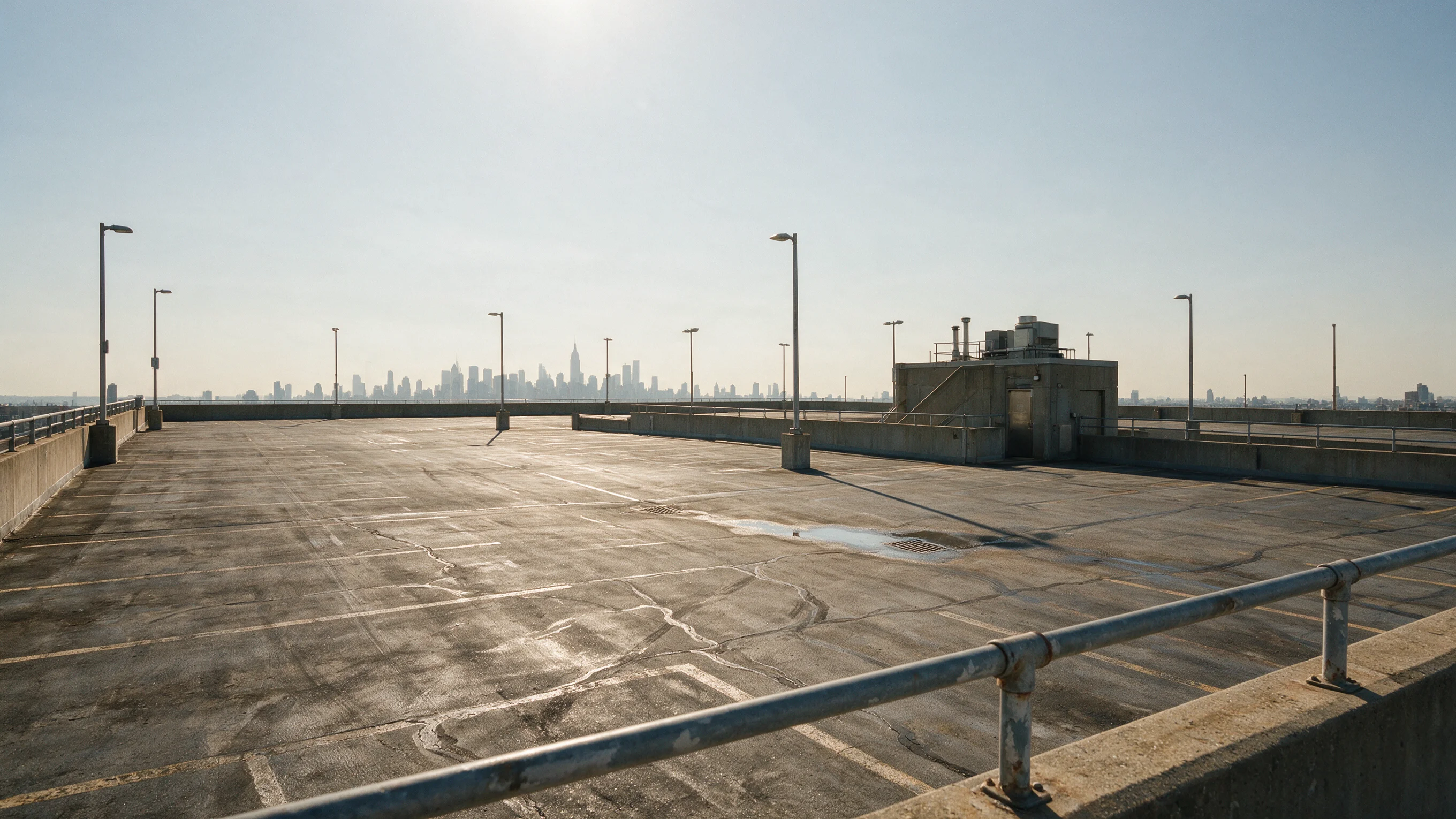 The open top deck of an empty concrete parking garage, light poles and a hazy New York skyline behind it